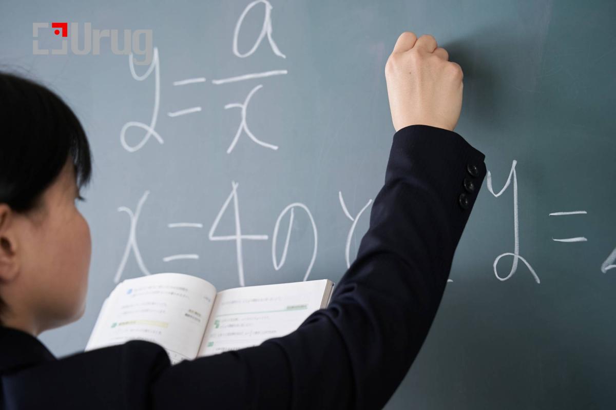 A Japanese woman teacher writes on the blackboard in her classroom
