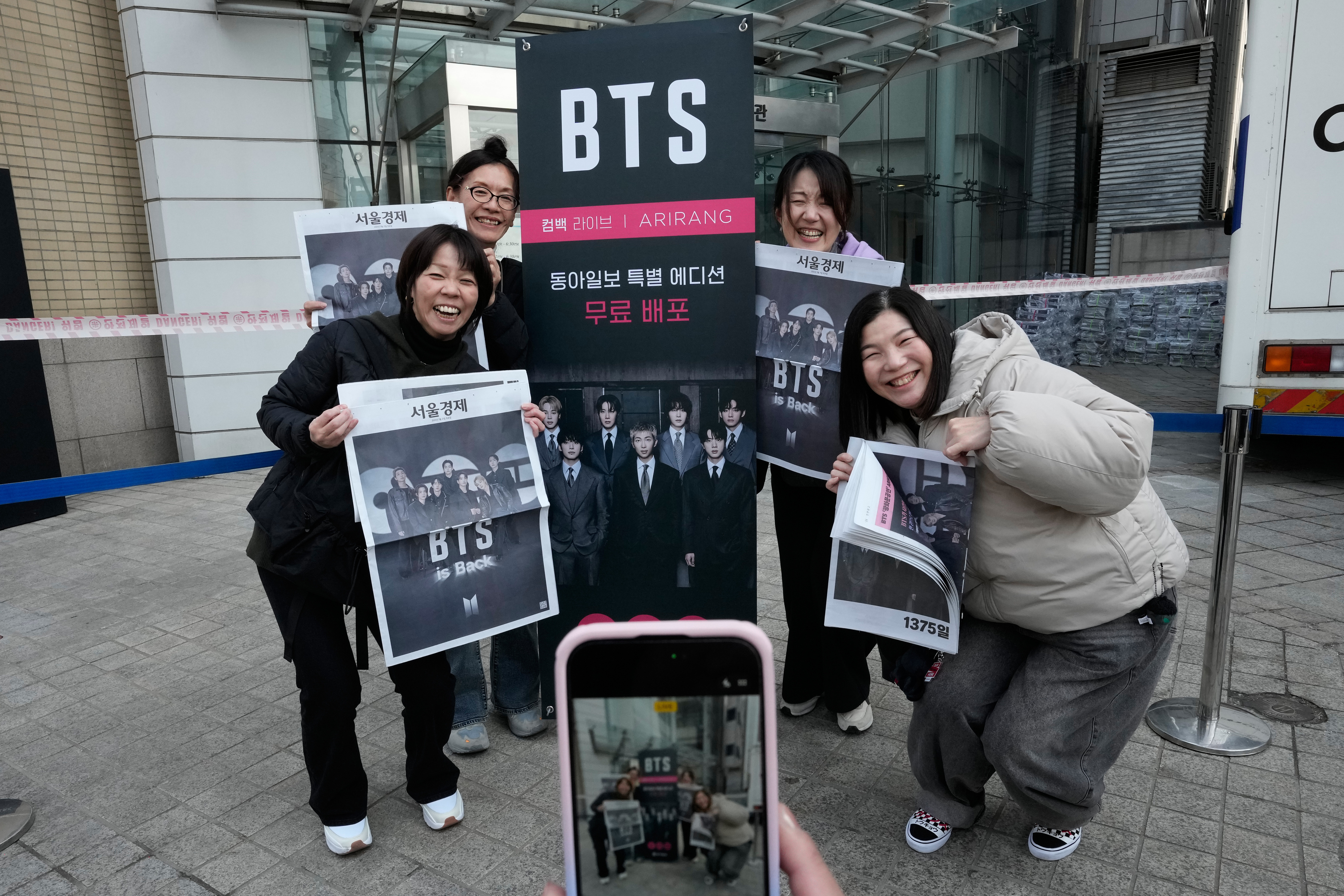 Fans of BTS poses with special edition of local news papers reporting the comeback of K-pop band BTS near Gwanghwamun Square in Seoul, South Korea, Saturday, March 21, 2026. (AP Photo/Ahn Young-joon)